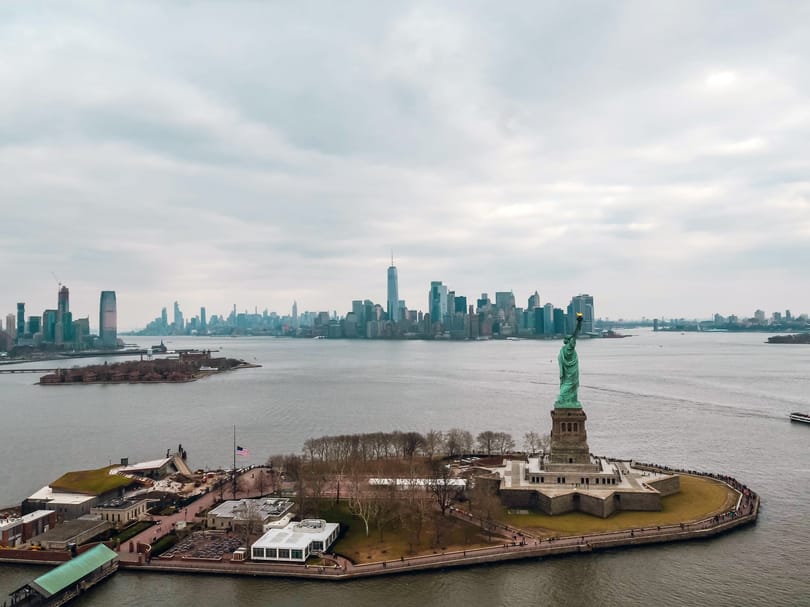 Aerial view of Liberty Island, the Statue of Liberty, New York Harbor, and the Lower Manhattan skyline in the distance.