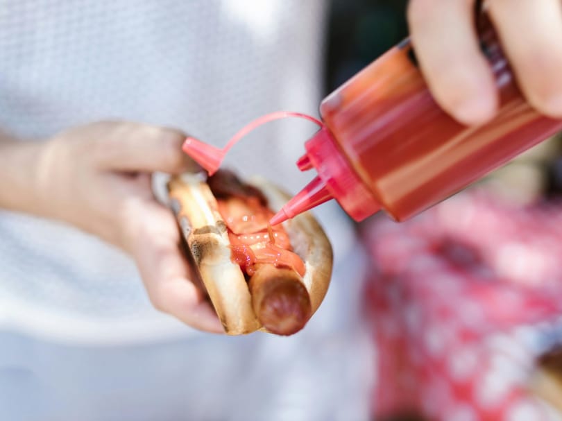 Person putting ketchup on hot dog