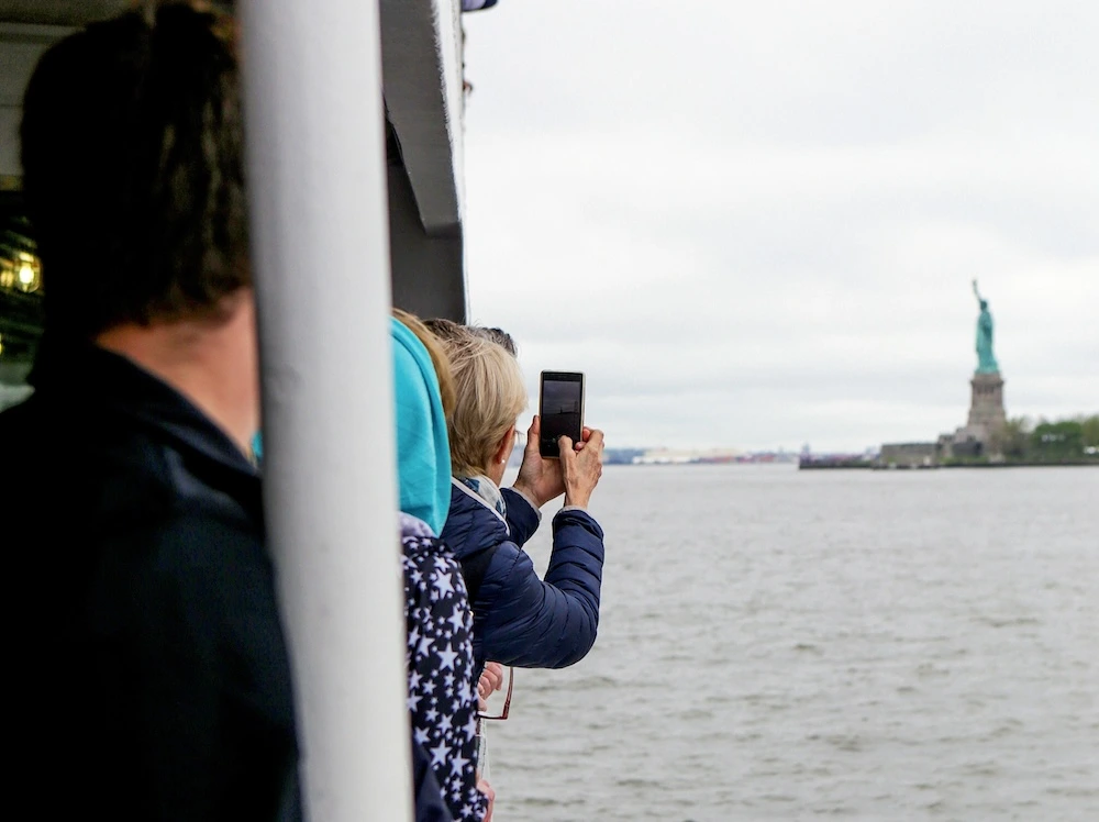 tourists on statue of liberty tour taking photos of the monument